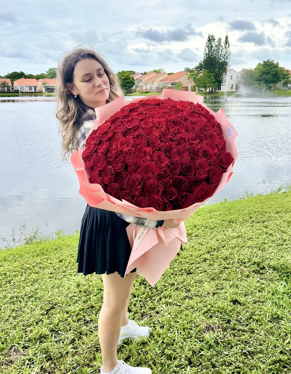 Woman holding a giant bouquet of 101 premium red roses with AVA Flowers sign in the background.