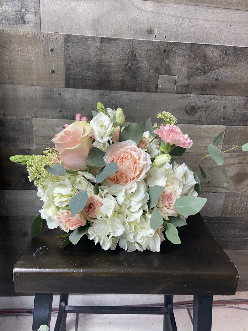 Elegant wedding flower arrangement featuring blush pink roses, white hydrangeas, lisianthus, and eucalyptus greenery, styled in a soft romantic design.