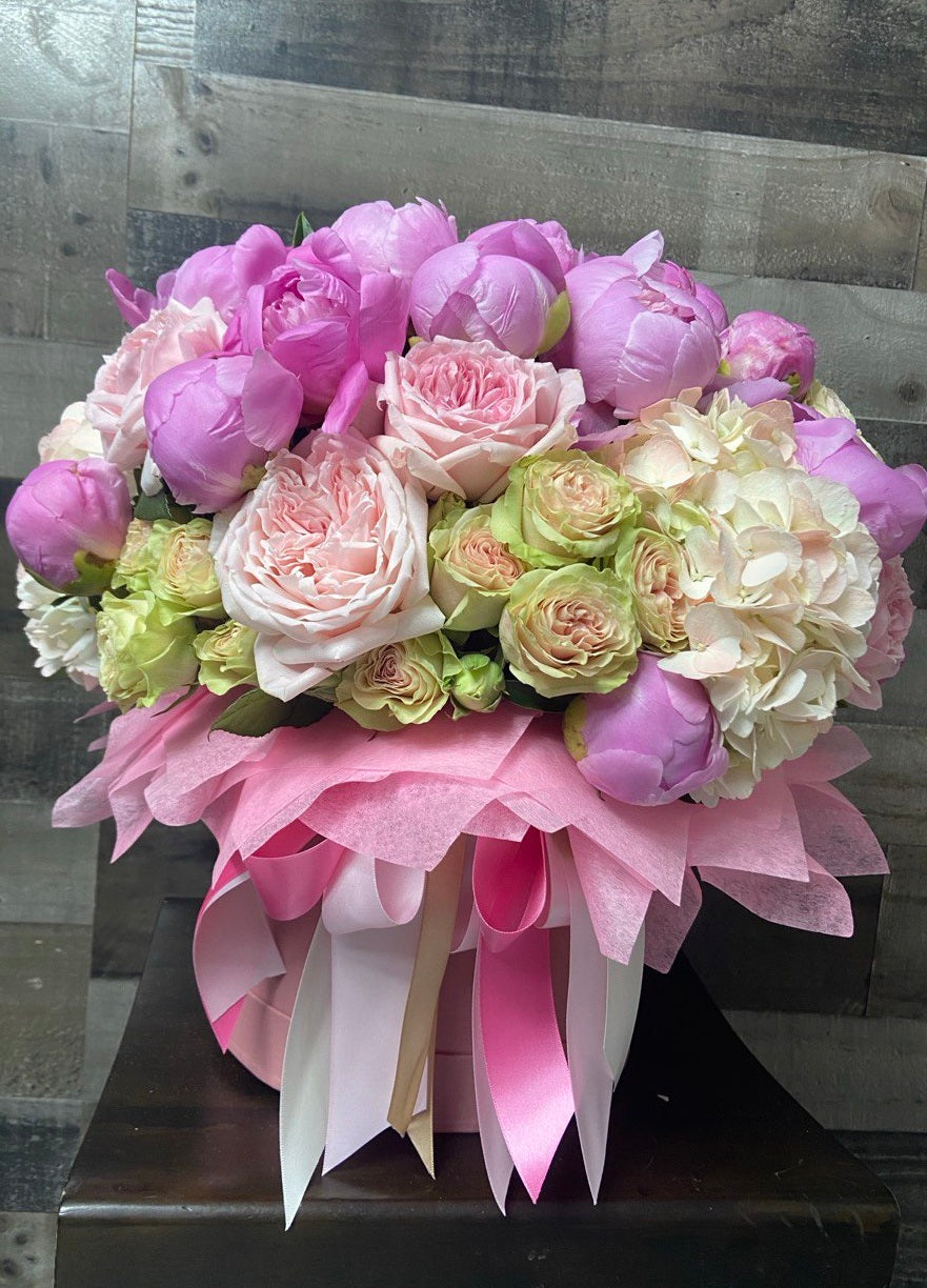 Luxurious hatbox arrangement with lush pink peonies, pastel garden roses, spray roses and hydrangeas, accented with decorative wrapping and satin ribbons.