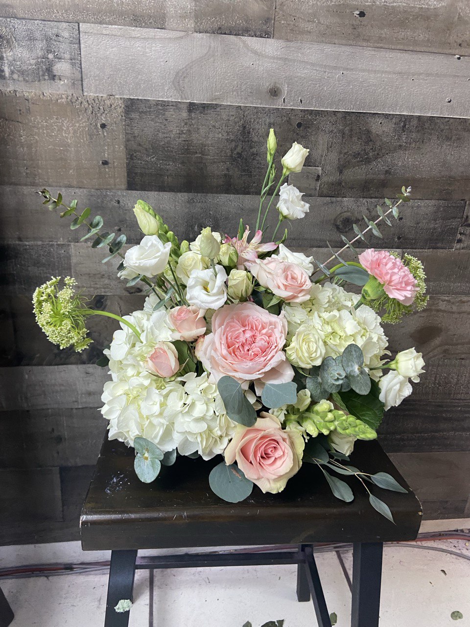 Elegant wedding flower arrangement featuring blush pink roses, white hydrangeas, lisianthus, and eucalyptus greenery, styled in a soft romantic design.