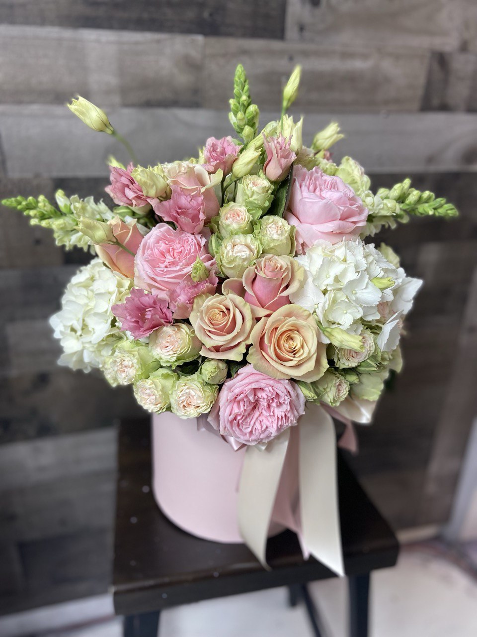 Elegant hatbox arrangement featuring pastel pink and cream roses, spray roses, lisianthus and white hydrangeas, styled with a satin ribbon for a romantic look.