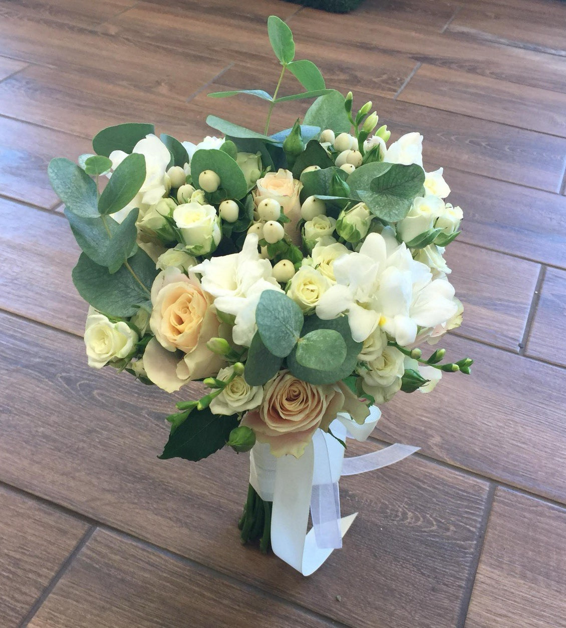 Bridal bouquet Pure Harmony with soft peach and cream roses, delicate white freesias, eucalyptus greenery, and elegant white ribbon for a timeless wedding look.