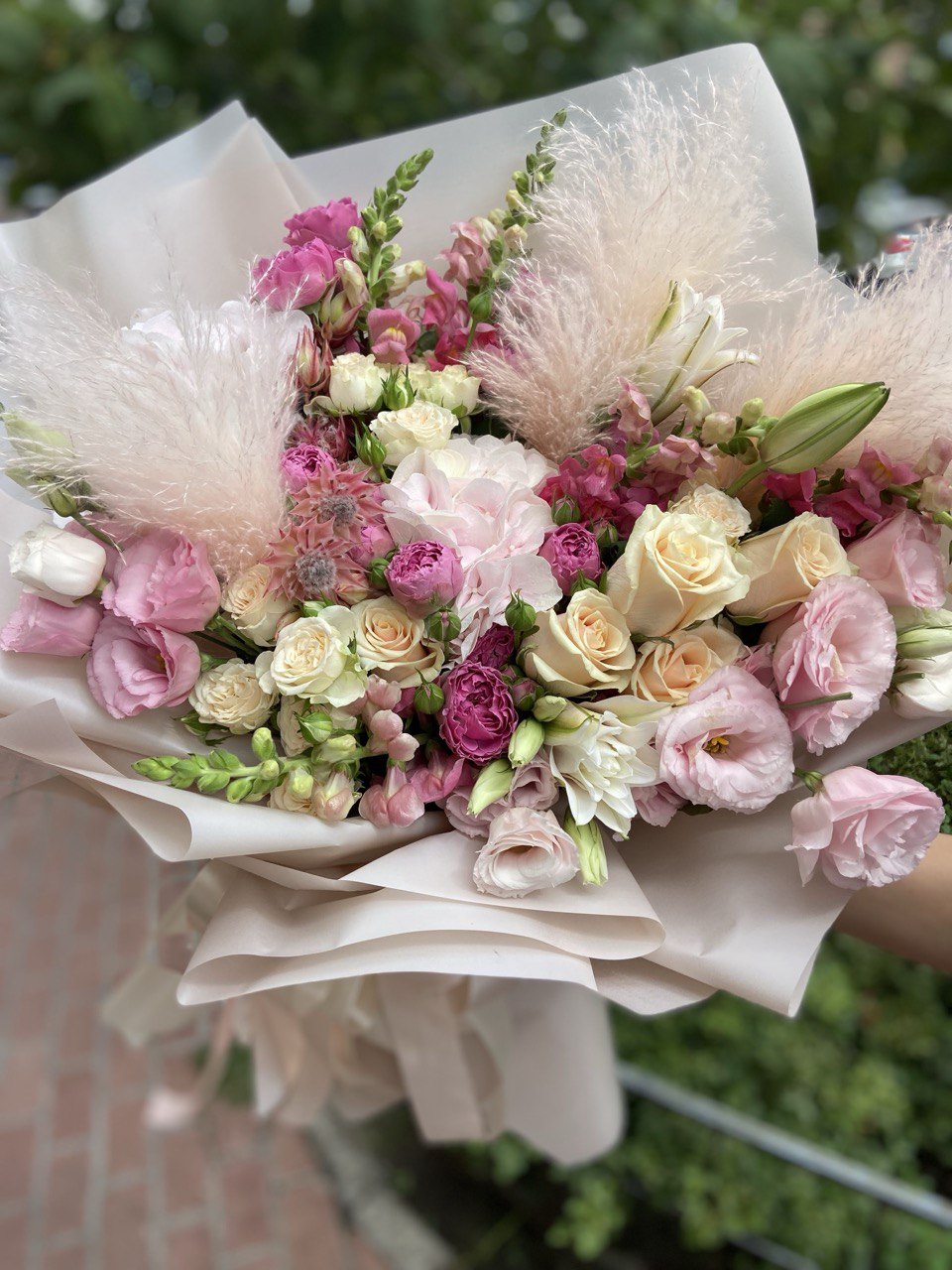 Tender Bliss bouquet with pastel roses, pink lisianthus, spray roses, lilies, and pampas grass wrapped in soft beige paper with satin ribbons — a delicate and romantic floral arrangement