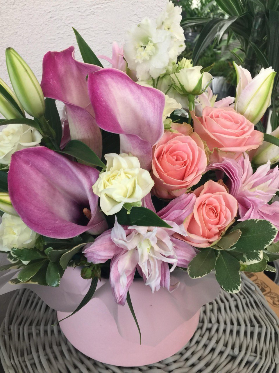 Delicate flower box arrangement featuring pink lilies, peach roses, white spray roses and purple calla lilies, styled in a soft pink designer box.