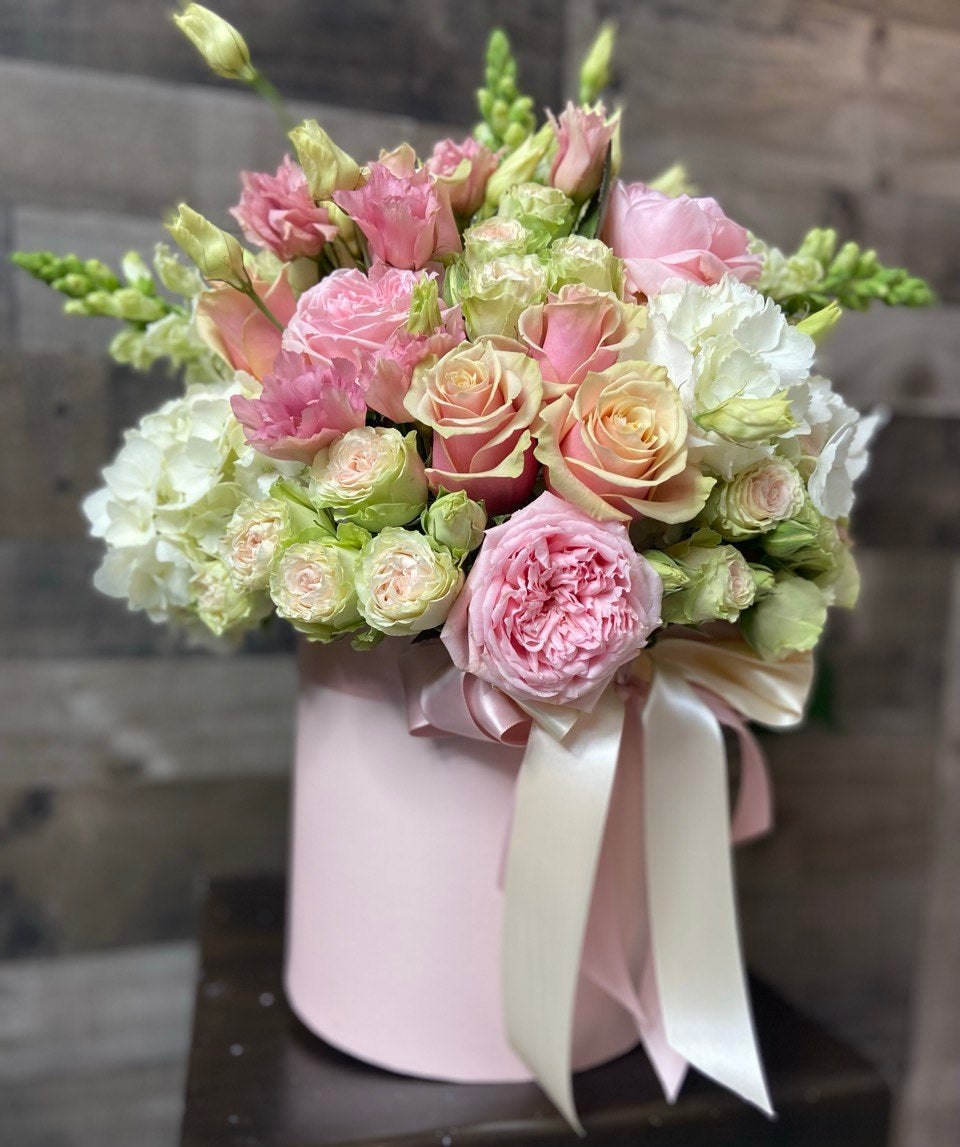Elegant hatbox arrangement featuring pastel pink and cream roses, spray roses, lisianthus and white hydrangeas, styled with a satin ribbon for a romantic look.