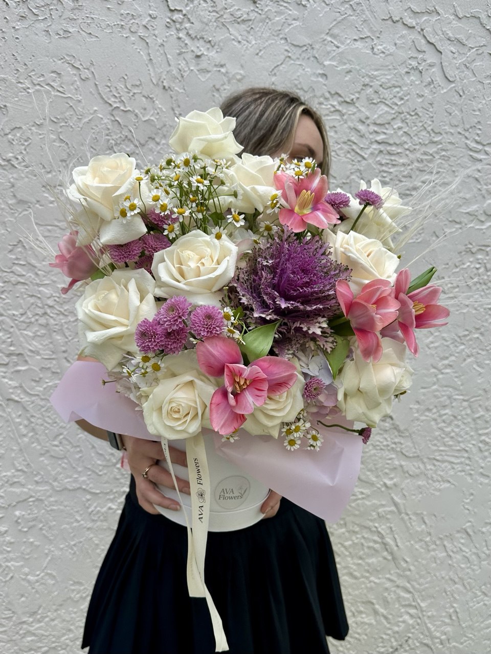 Person holding a bouquet of flowers against a textured white wall