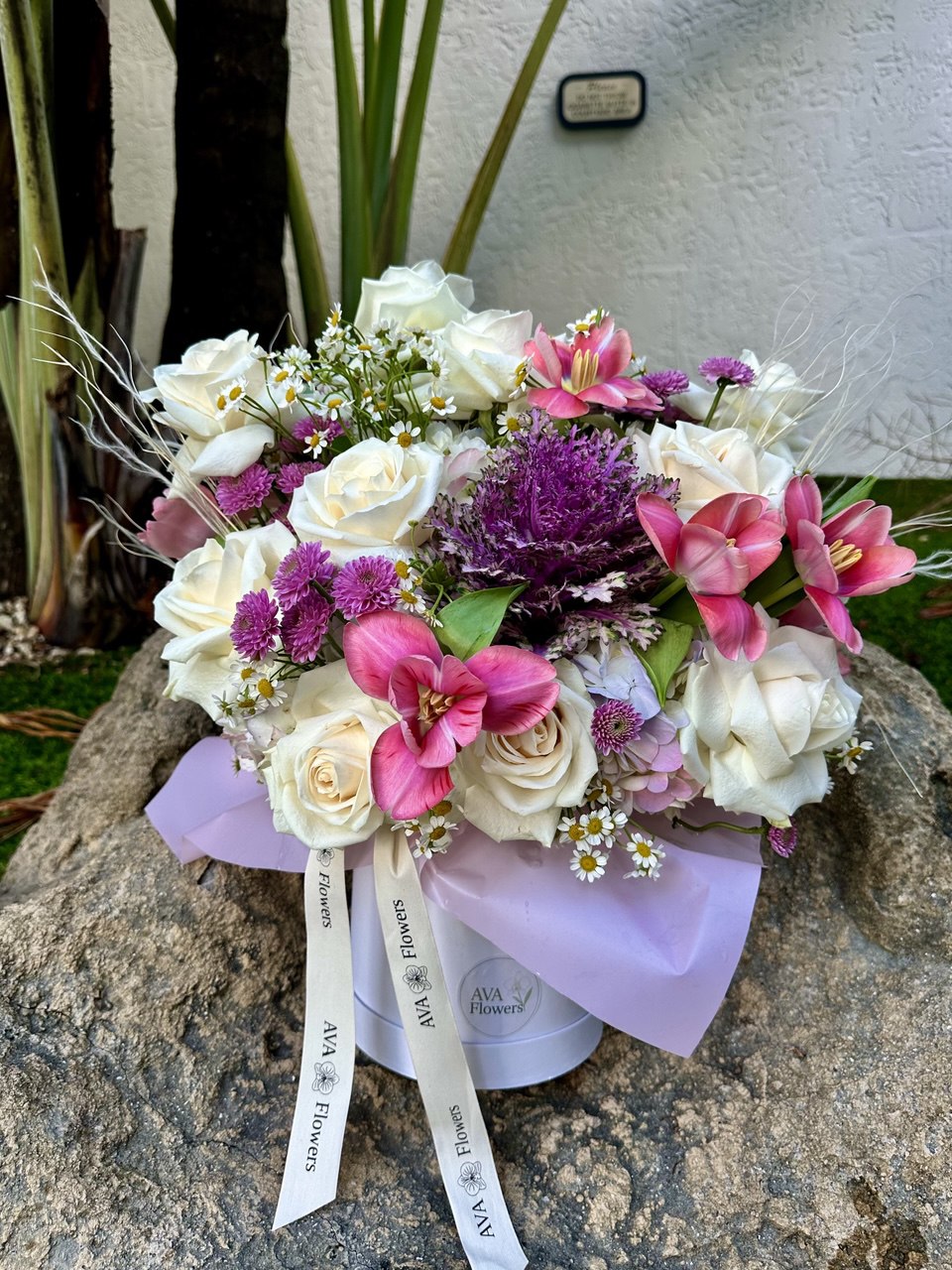 Bouquet of flowers in a white container with pink and purple accents on a stone surface.