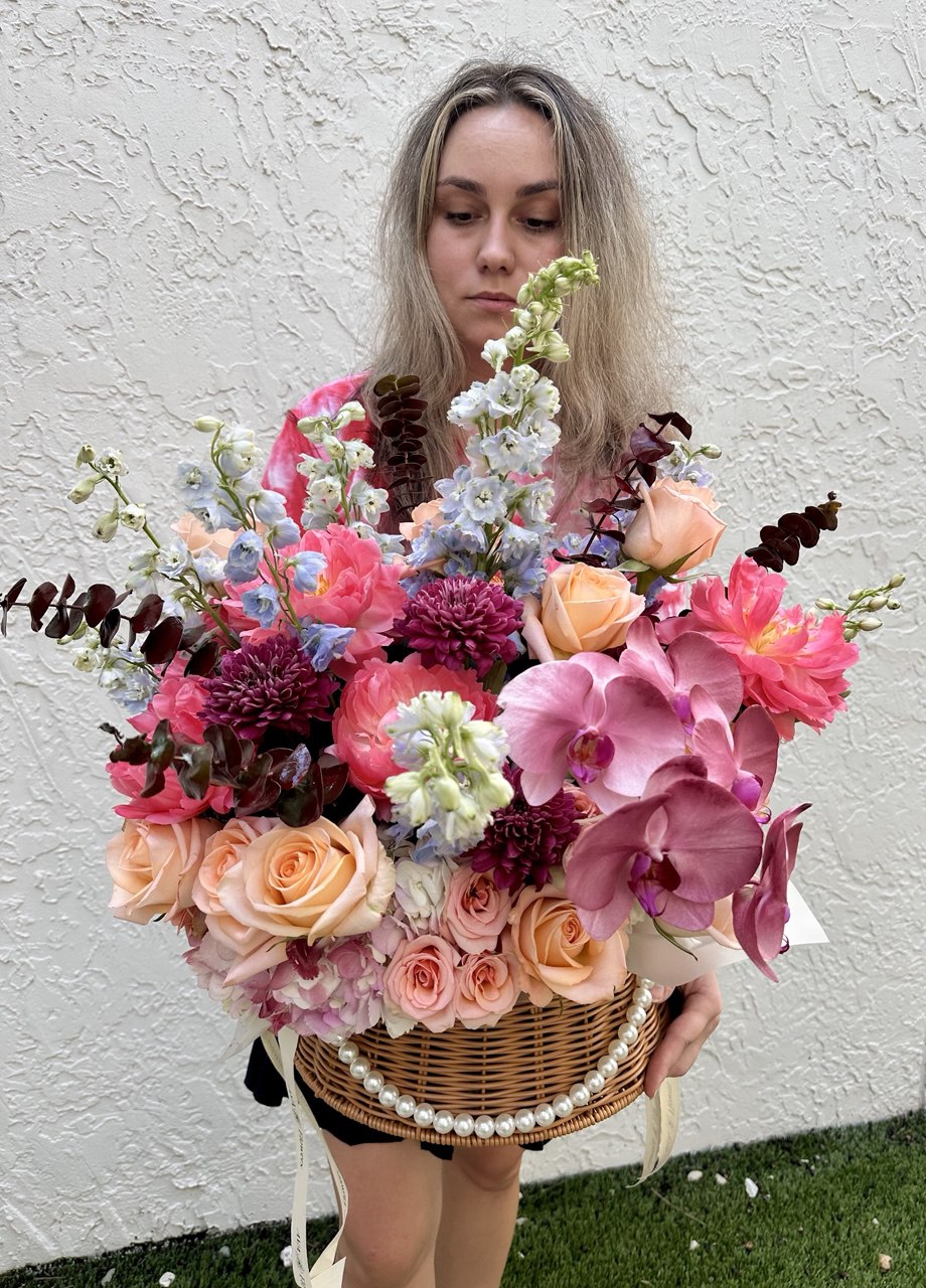 Woman holding a large, colorful bouquet of flowers against a white wall.