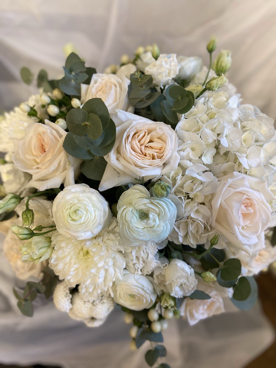 Elegant hatbox flower arrangement with white roses, ranunculus, hydrangeas, chrysanthemums and eucalyptus, creating a fresh and timeless design.