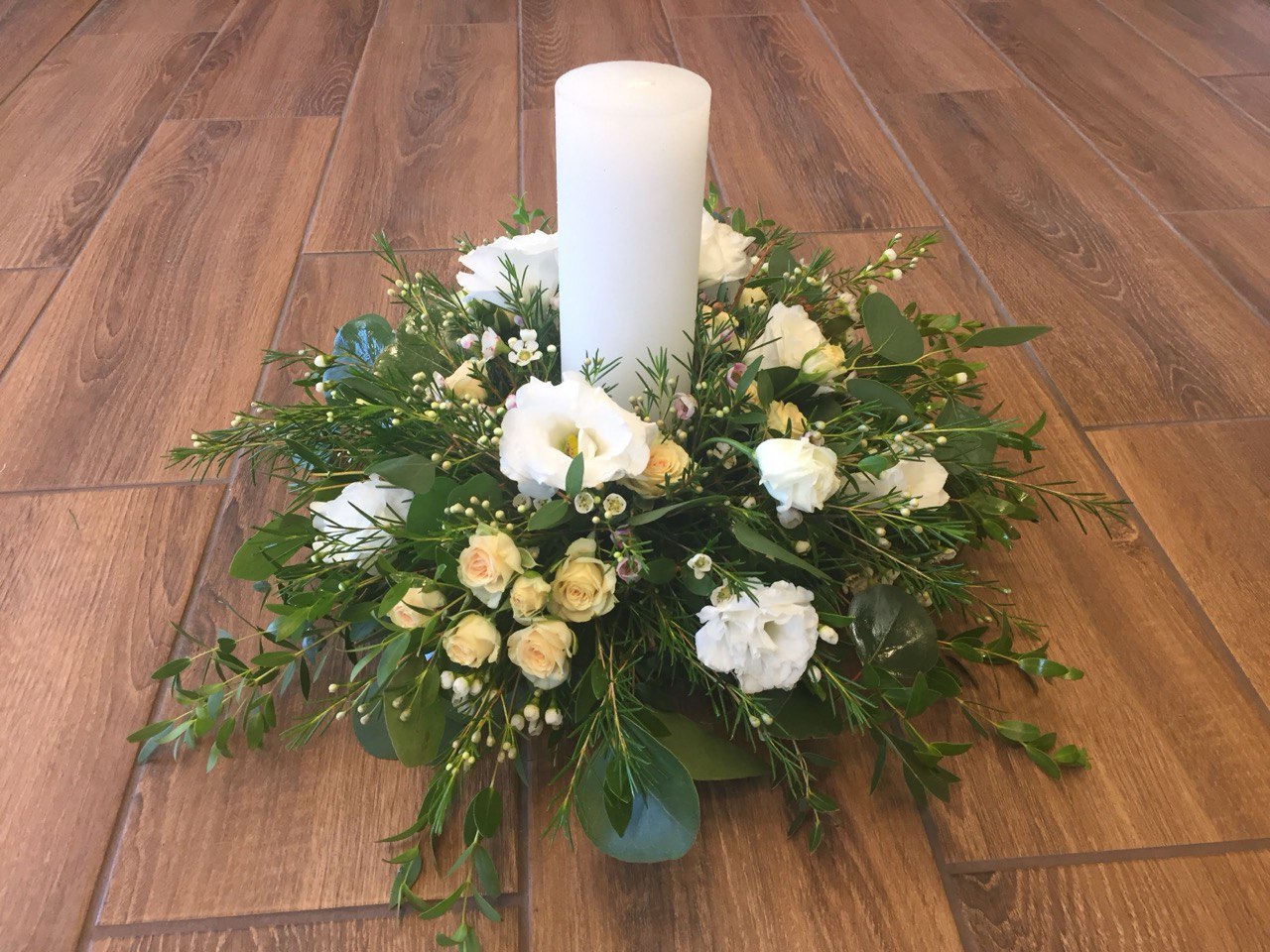 Elegant centerpiece with white flowers, lush greenery, and a tall white candle, perfect for weddings, receptions, or home décor.