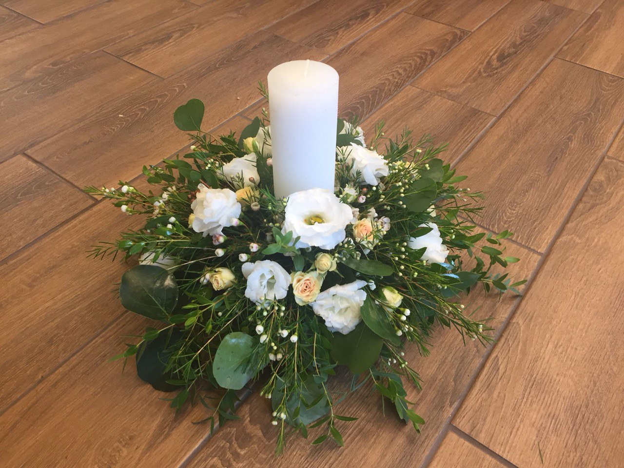 Elegant centerpiece with white flowers, lush greenery, and a tall white candle, perfect for weddings, receptions, or home décor.