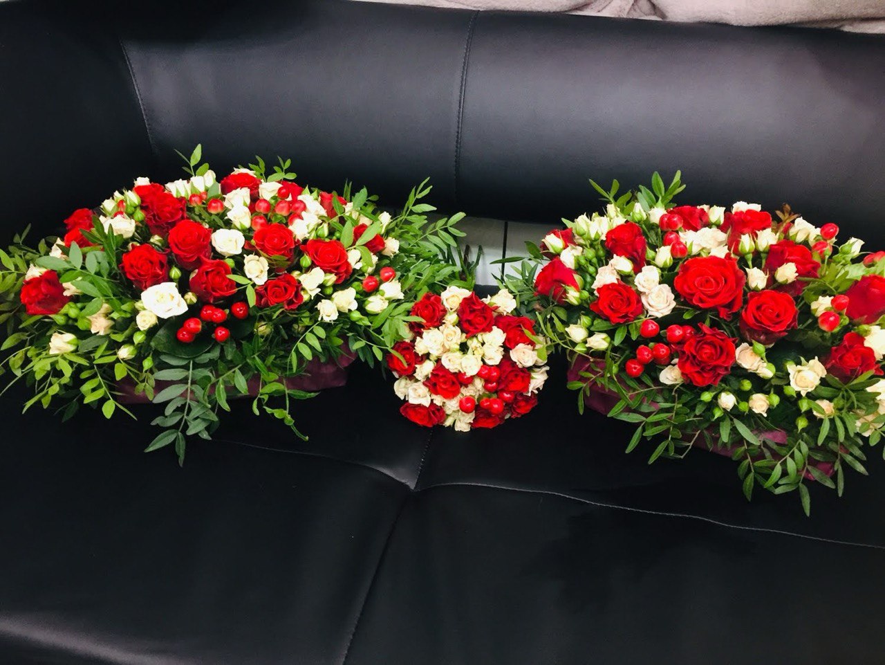 Three elegant floral arrangements with red and white roses, hypericum berries, and lush greenery, beautifully displayed on a black background.