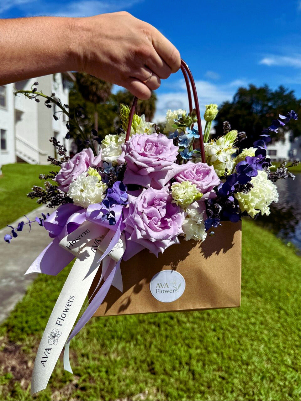 Hand holding a bouquet of flowers with a visible brand label against a green outdoor background
