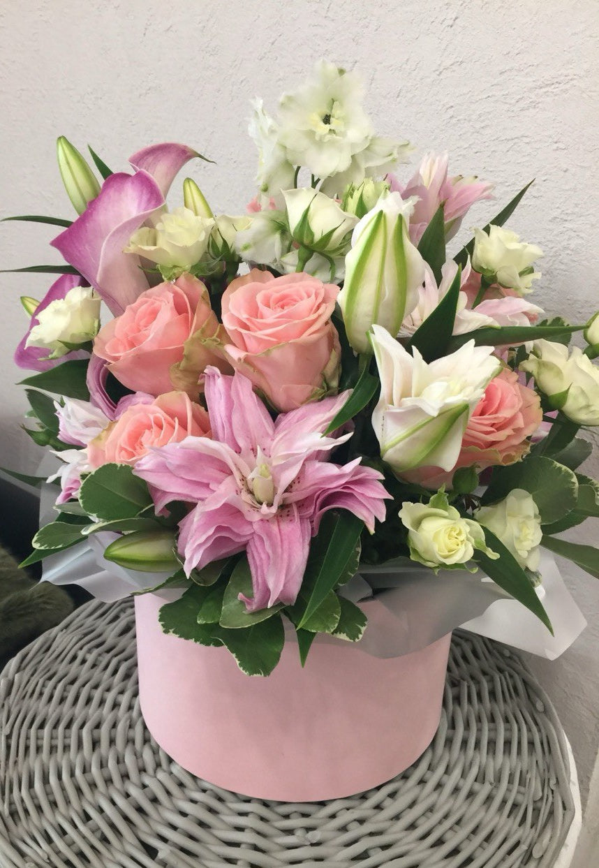 Delicate flower box arrangement featuring pink lilies, peach roses, white spray roses and purple calla lilies, styled in a soft pink designer box.