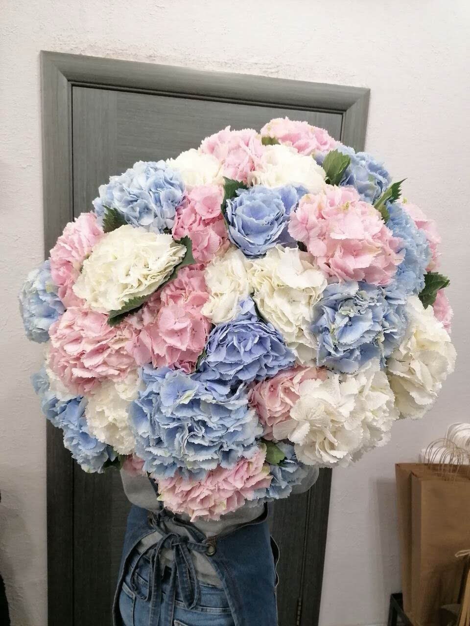 A large round bouquet of fresh hydrangeas in soft pastel shades of white, pink, and blue, arranged in a lush and elegant style