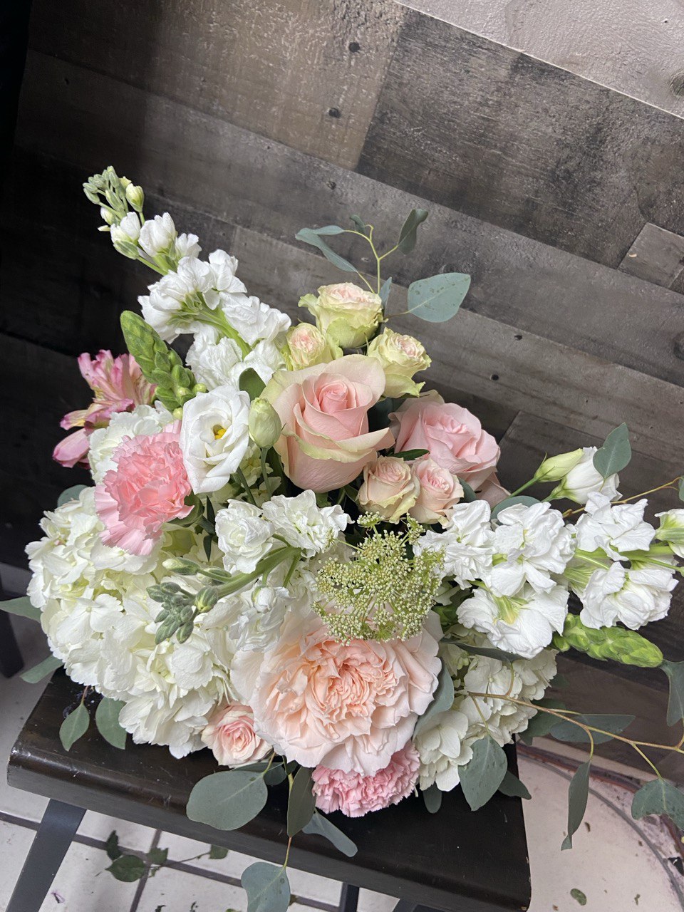 Elegant wedding flower arrangement featuring blush pink roses, white hydrangeas, lisianthus, and eucalyptus greenery, styled in a soft romantic design.