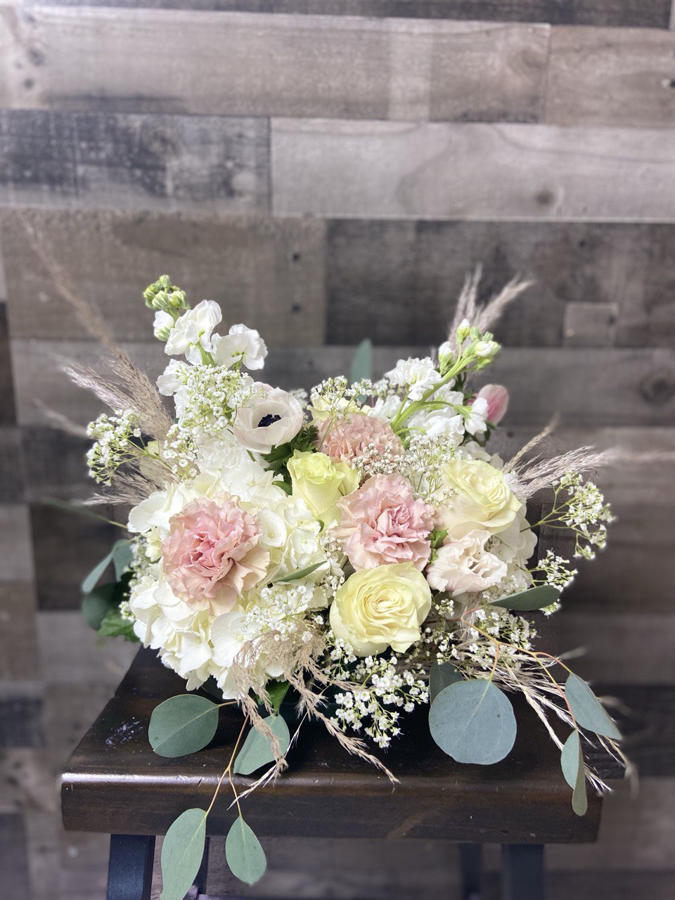 Elegant wedding flower arrangement featuring blush pink roses, white hydrangeas, lisianthus, and eucalyptus greenery, styled in a soft romantic design.