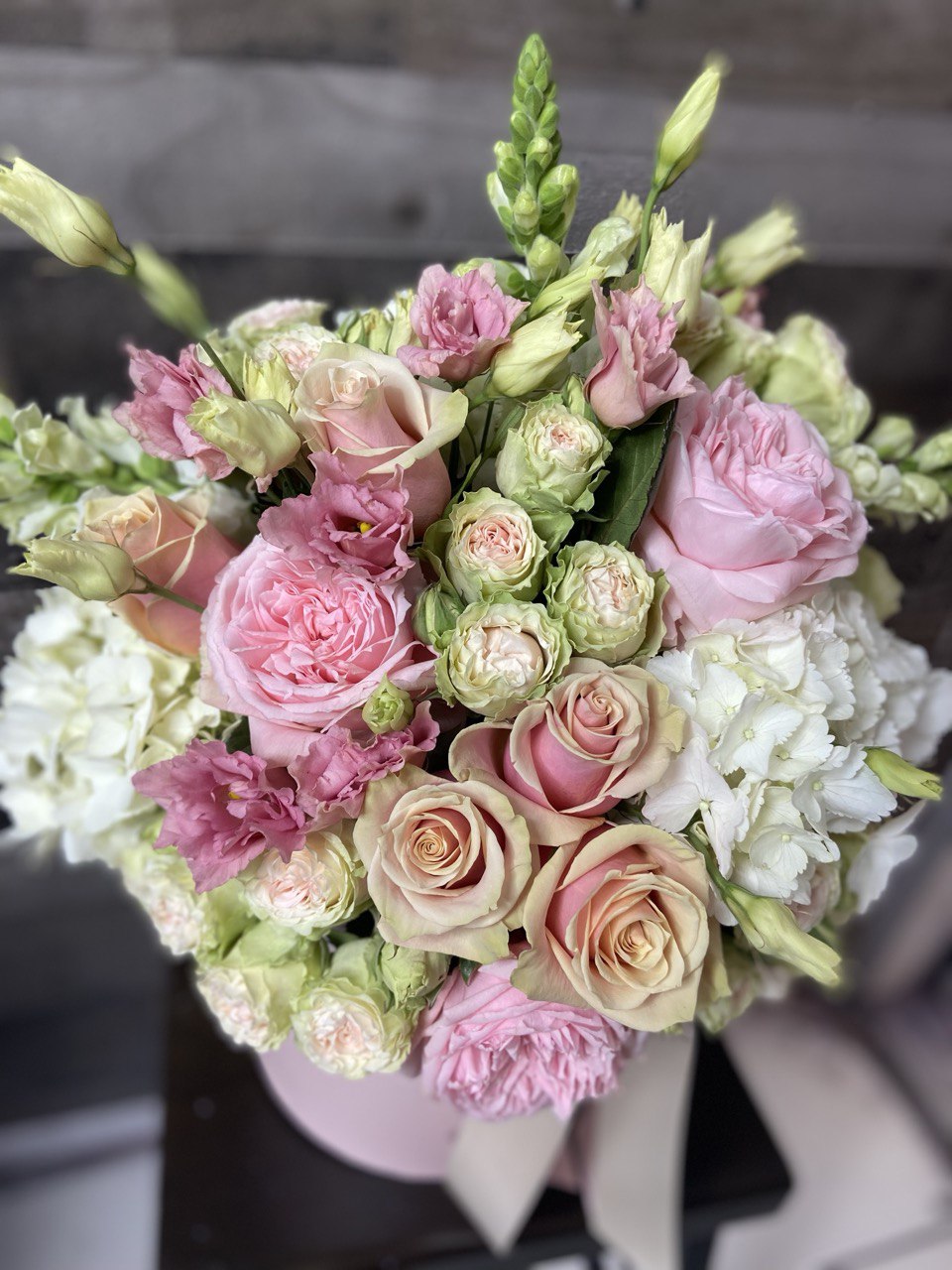 Elegant hatbox arrangement featuring pastel pink and cream roses, spray roses, lisianthus and white hydrangeas, styled with a satin ribbon for a romantic look.