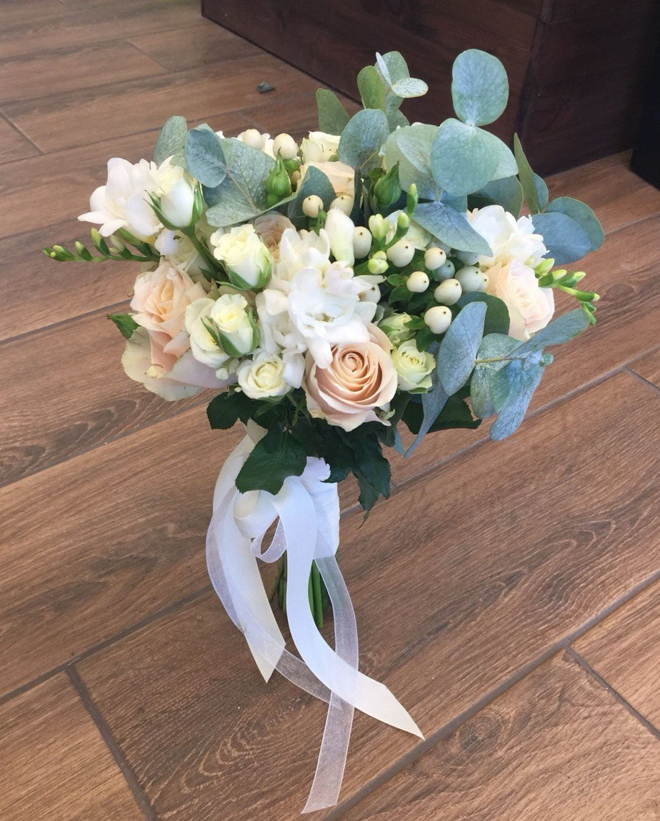 Bridal bouquet Pure Harmony with soft peach and cream roses, delicate white freesias, eucalyptus greenery, and elegant white ribbon for a timeless wedding look.