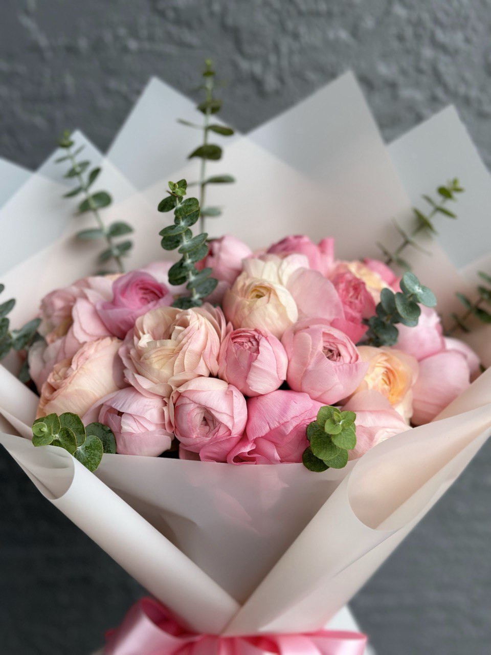 Mono bouquet of pink ranunculus with fresh eucalyptus, wrapped in white paper and tied with a pink satin ribbon — an elegant and romantic floral gift.