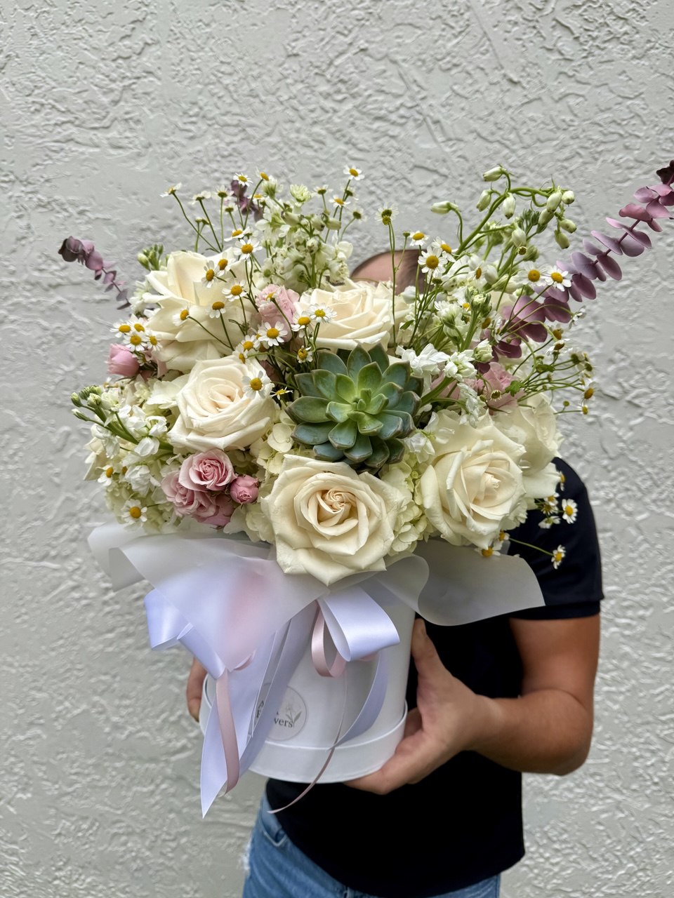 Person holding a bouquet of flowers in a white box against a gray background