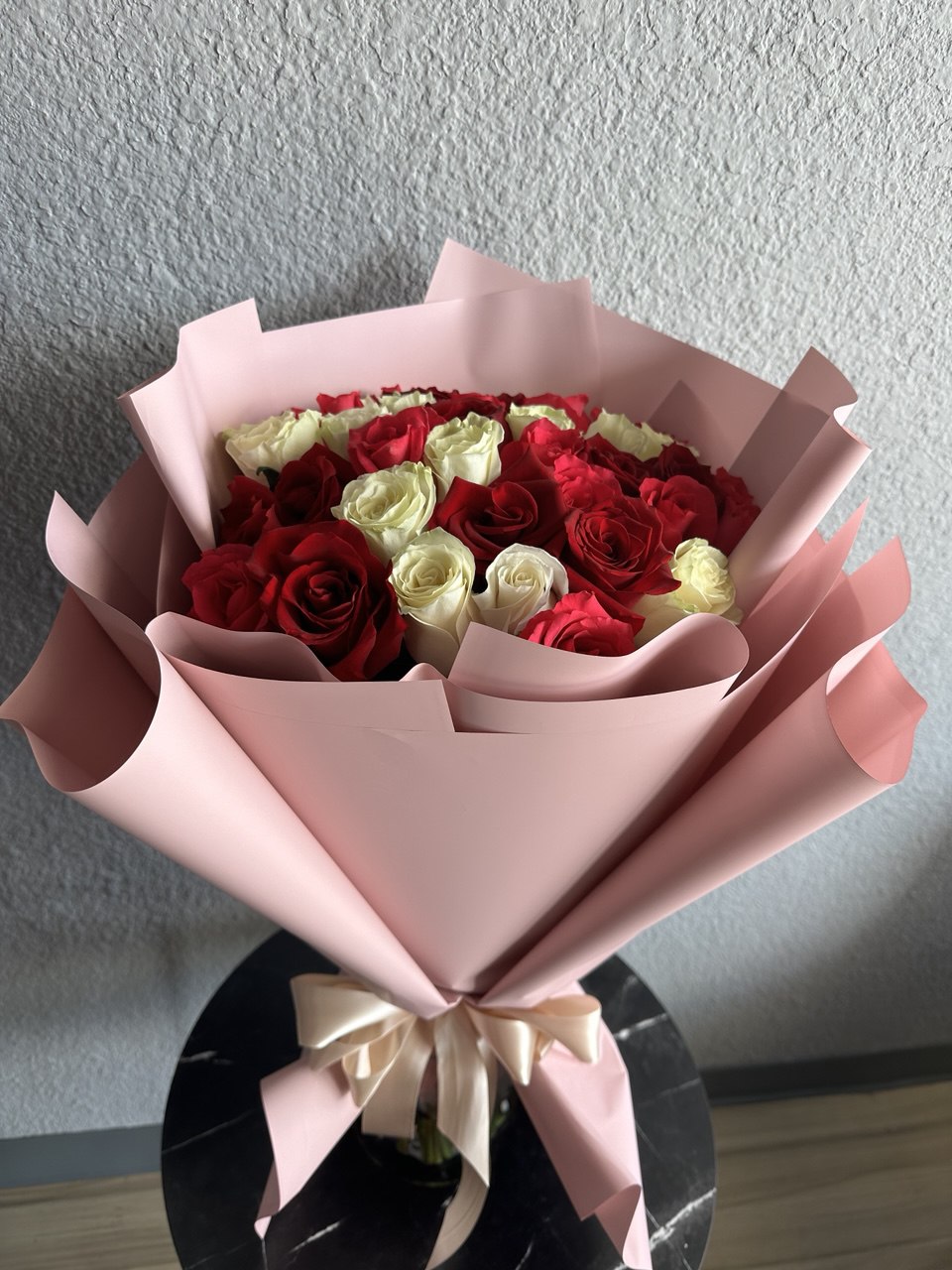 Romantic bouquet with fresh red and white roses, arranged in soft pink designer wrapping and tied with a satin ribbon, symbolizing love and elegance.