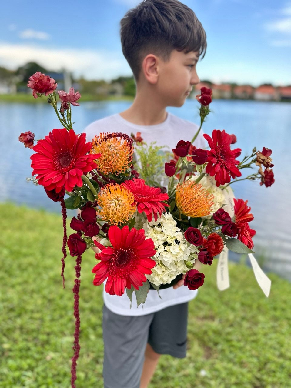 Scarlet Charm flower composition with vibrant red gerberas, exotic orange pincushion protea, white hydrangea, spray roses, and seasonal blooms in a stylish vase — a bold and elegant floral arrangement.