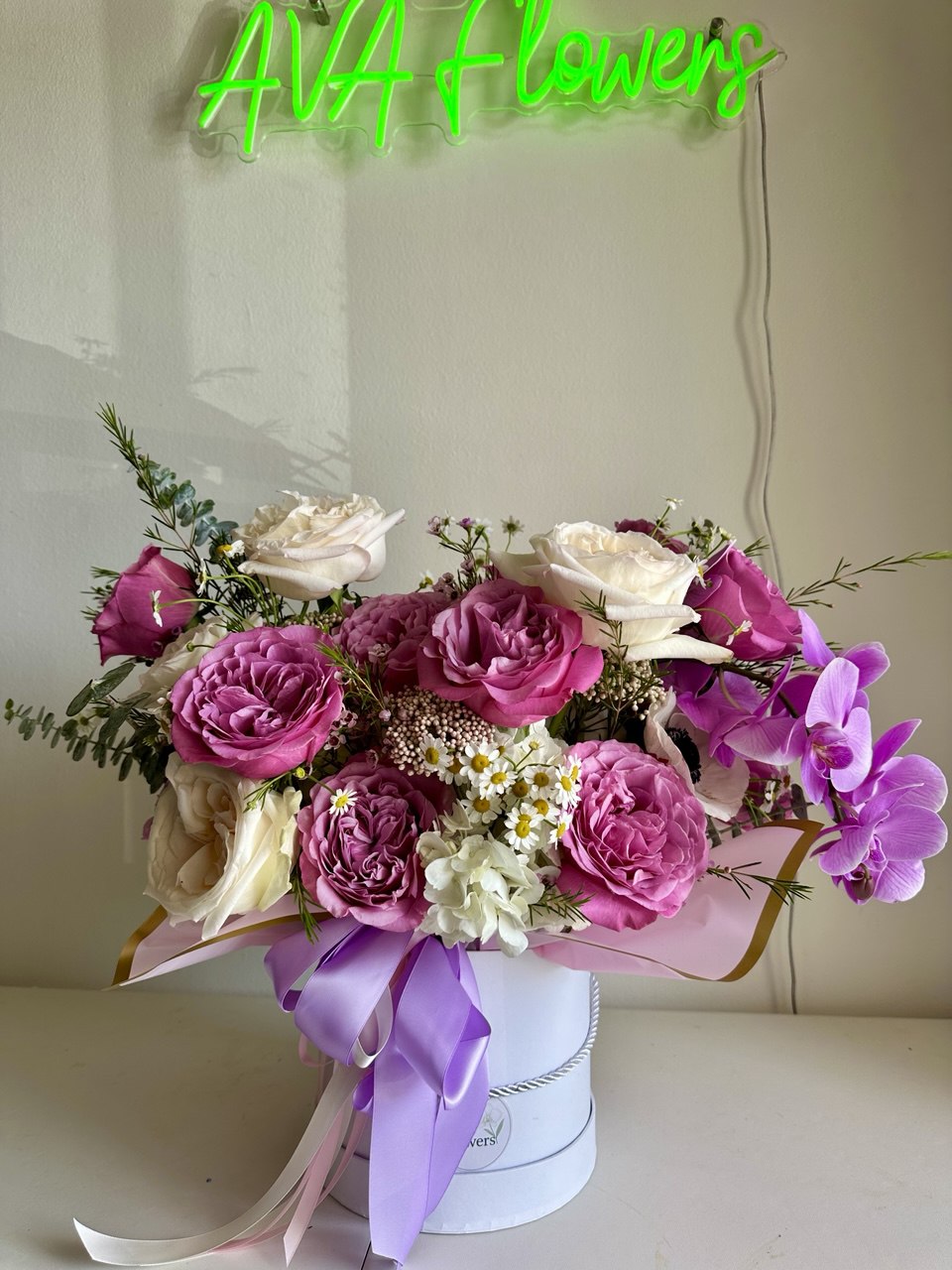 Aurora Hat Box flower arrangement with lush pink and cream roses, delicate orchids, anemones, chamomile, and eucalyptus greenery in an elegant white hat box tied with pastel ribbons — a luxurious floral gift