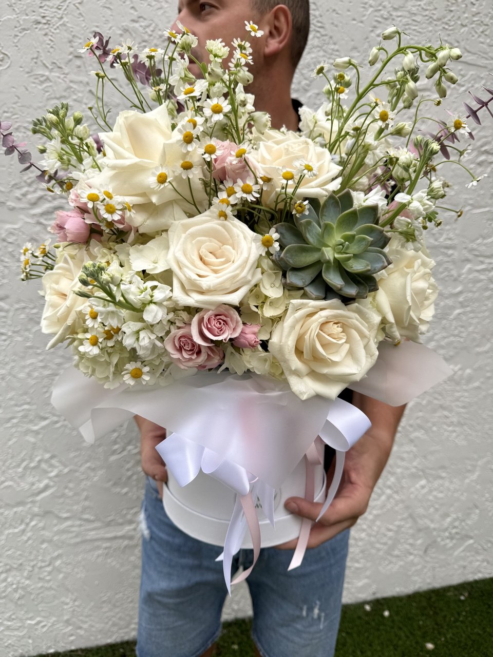 Person holding a bouquet of flowers with white roses, pink roses, and succulents against a plain background.