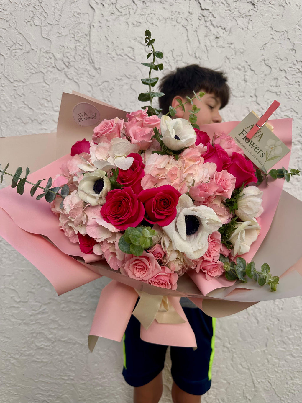 Child holding a large bouquet of flowers with a visible brand name on a textured wall background