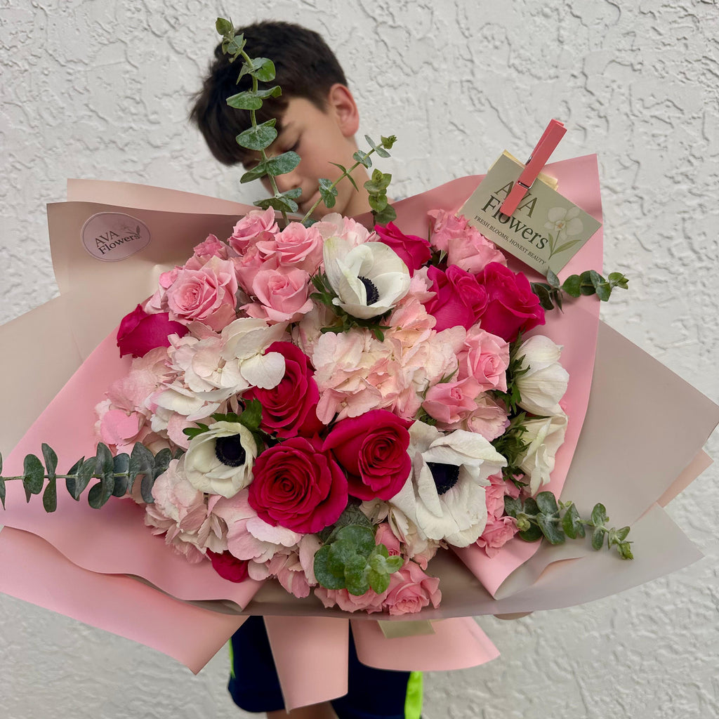 Child holding a bouquet of flowers with a visible brand tag against a textured white wall.