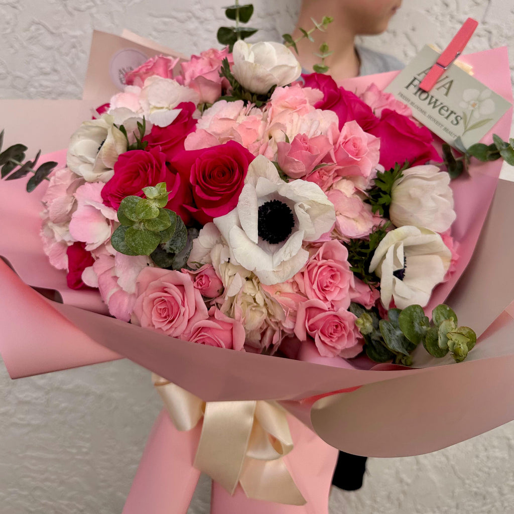 Bouquet of flowers with a person holding it against a textured wall.