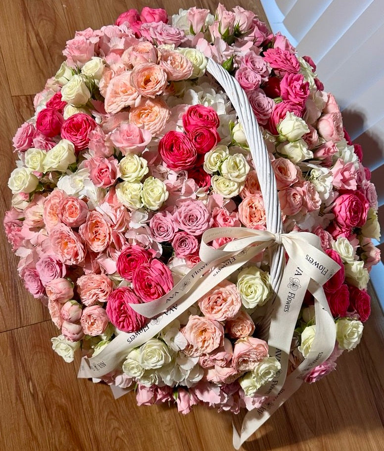 Round arrangement of pink, white, and red roses with a white ribbon on a wooden surface.
