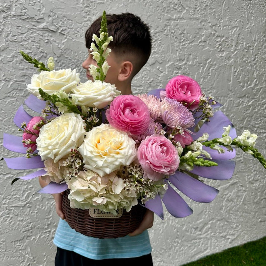 Child holding a large bouquet of flowers against a plain wall.