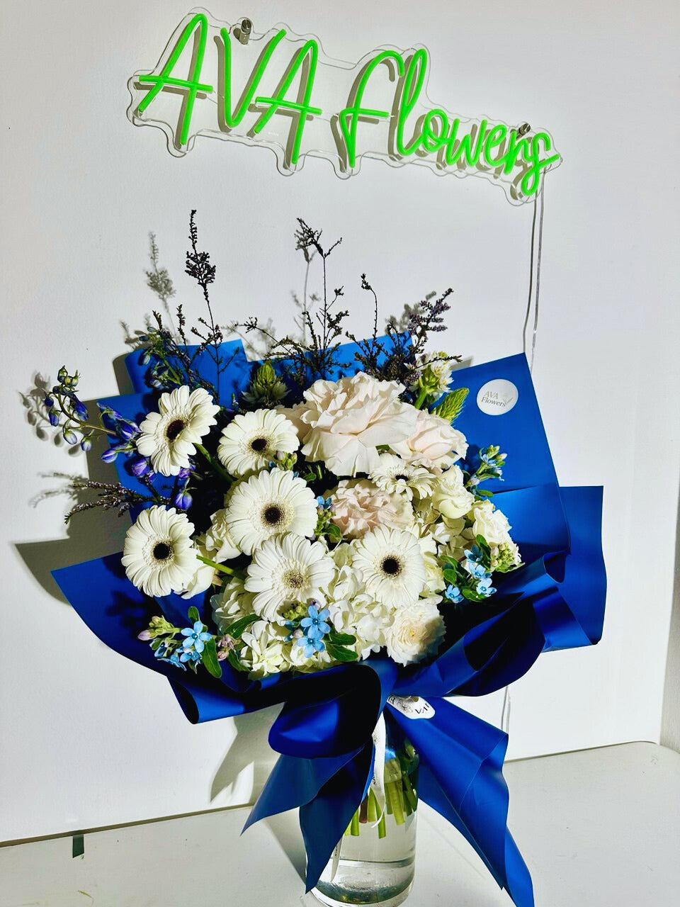 Bouquet of flowers with blue ribbons in front of an 'AVA Flowers' sign.