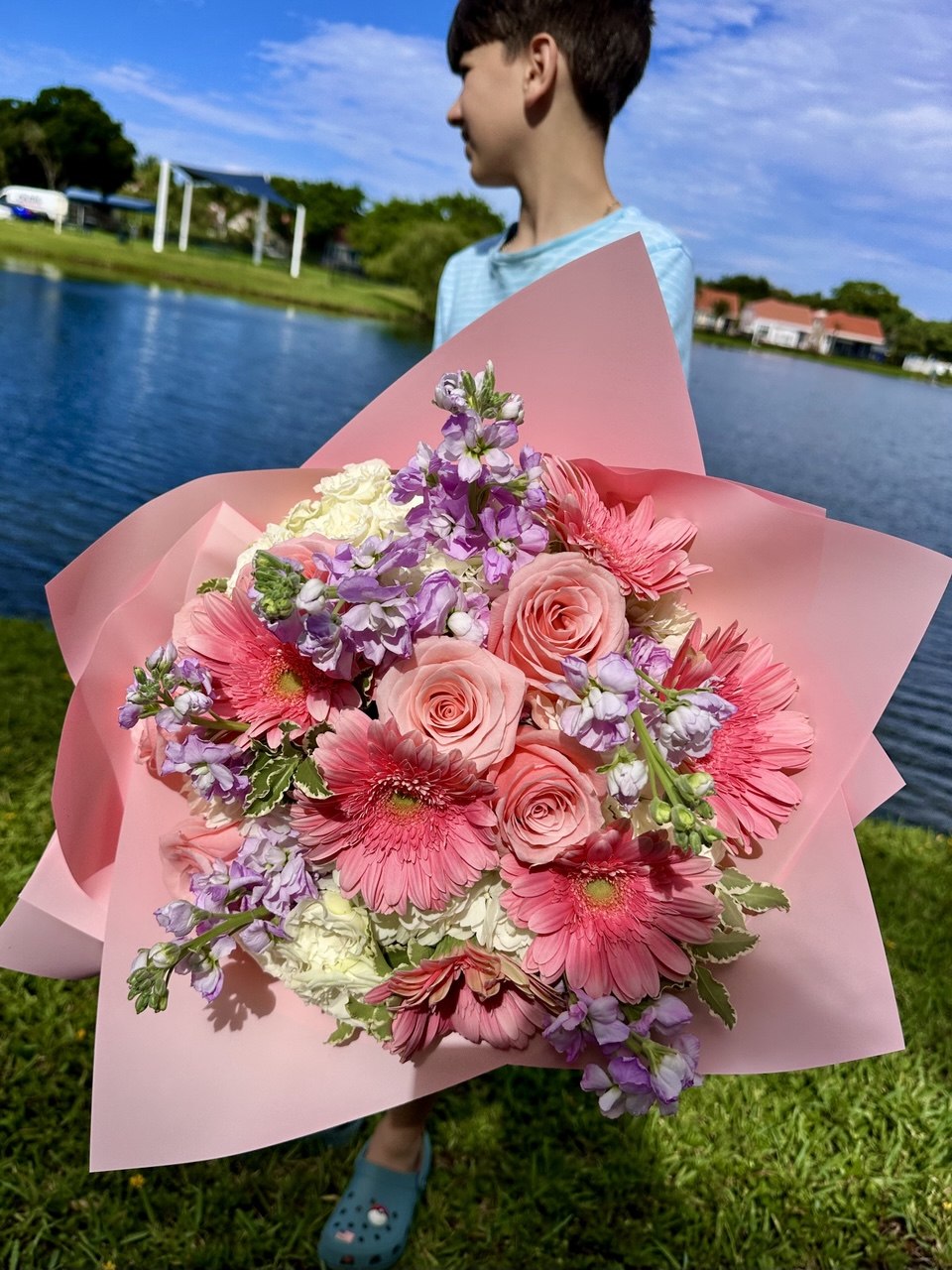 Person holding a large bouquet of flowers outdoors by a lake