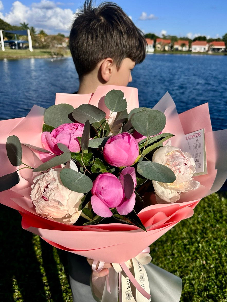 Person holding a bouquet of pink flowers by a lake