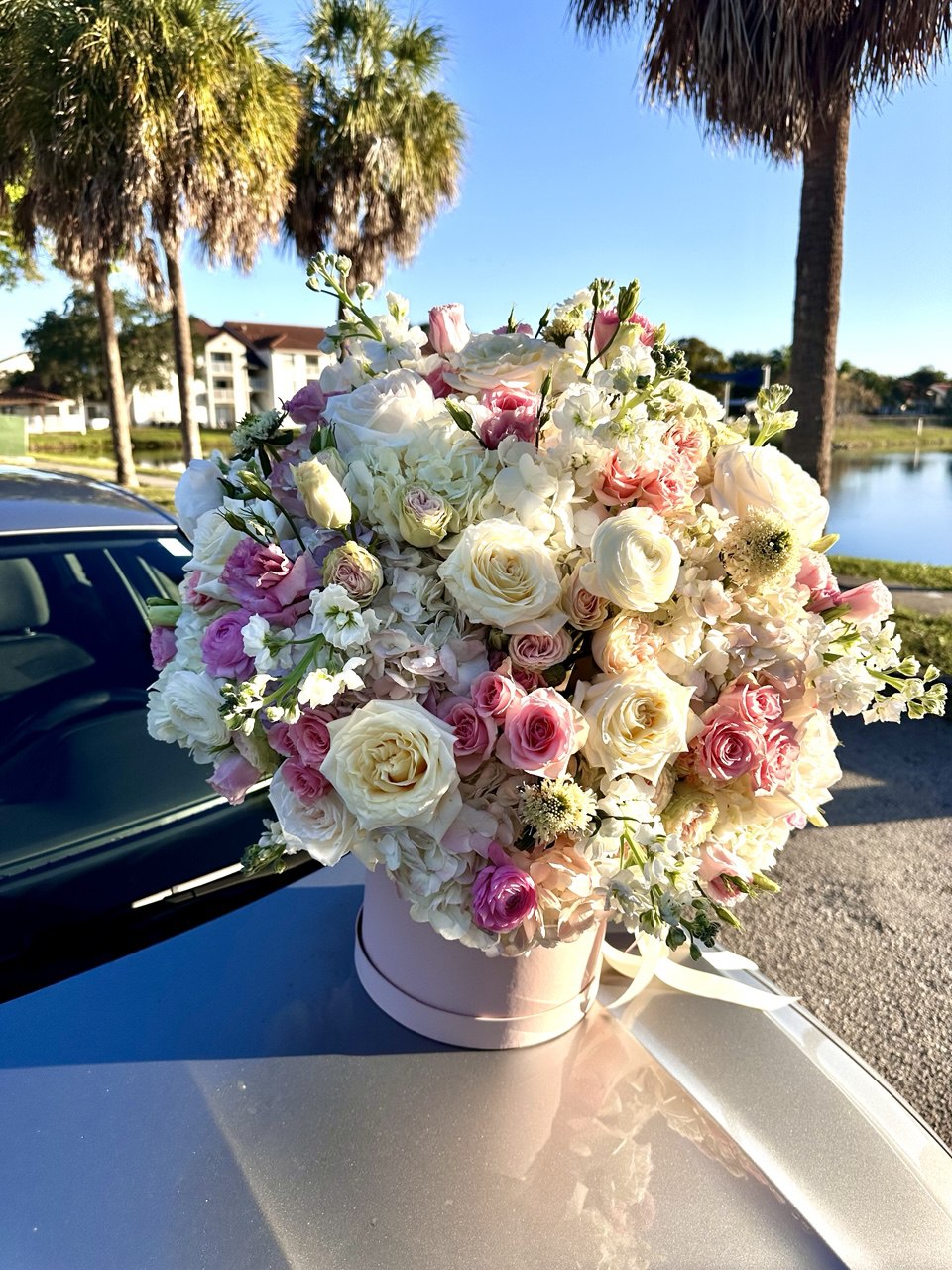 Floral arrangement in a pink box on a car hood with palm trees and a lake in the background