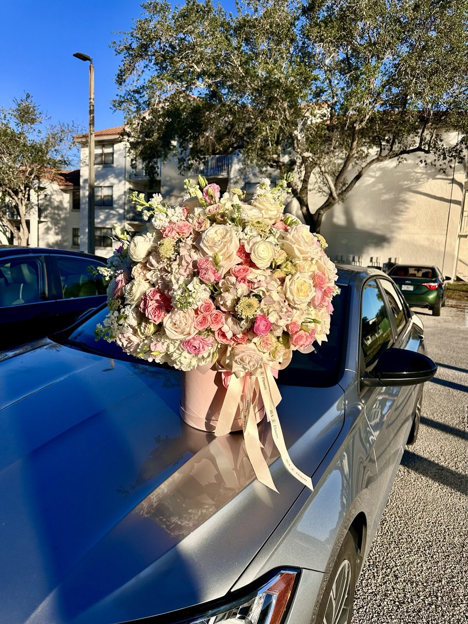 Bouquet of flowers on a car hood with a building and trees in the background