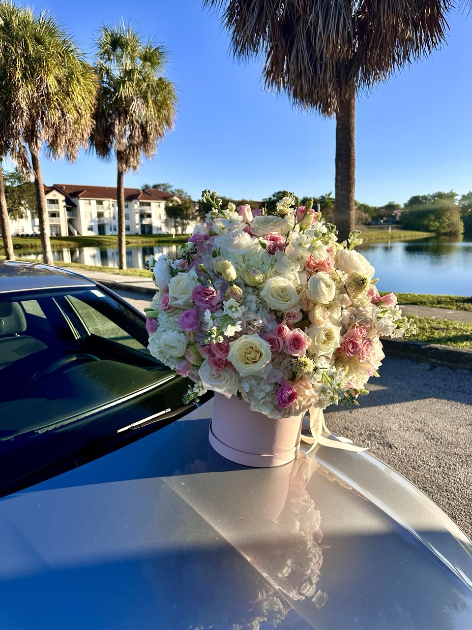 Floral arrangement on a car hood with palm trees and a lake in the background