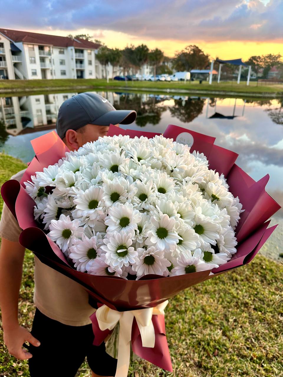 Person holding a large bouquet of white flowers by a lake with buildings in the background