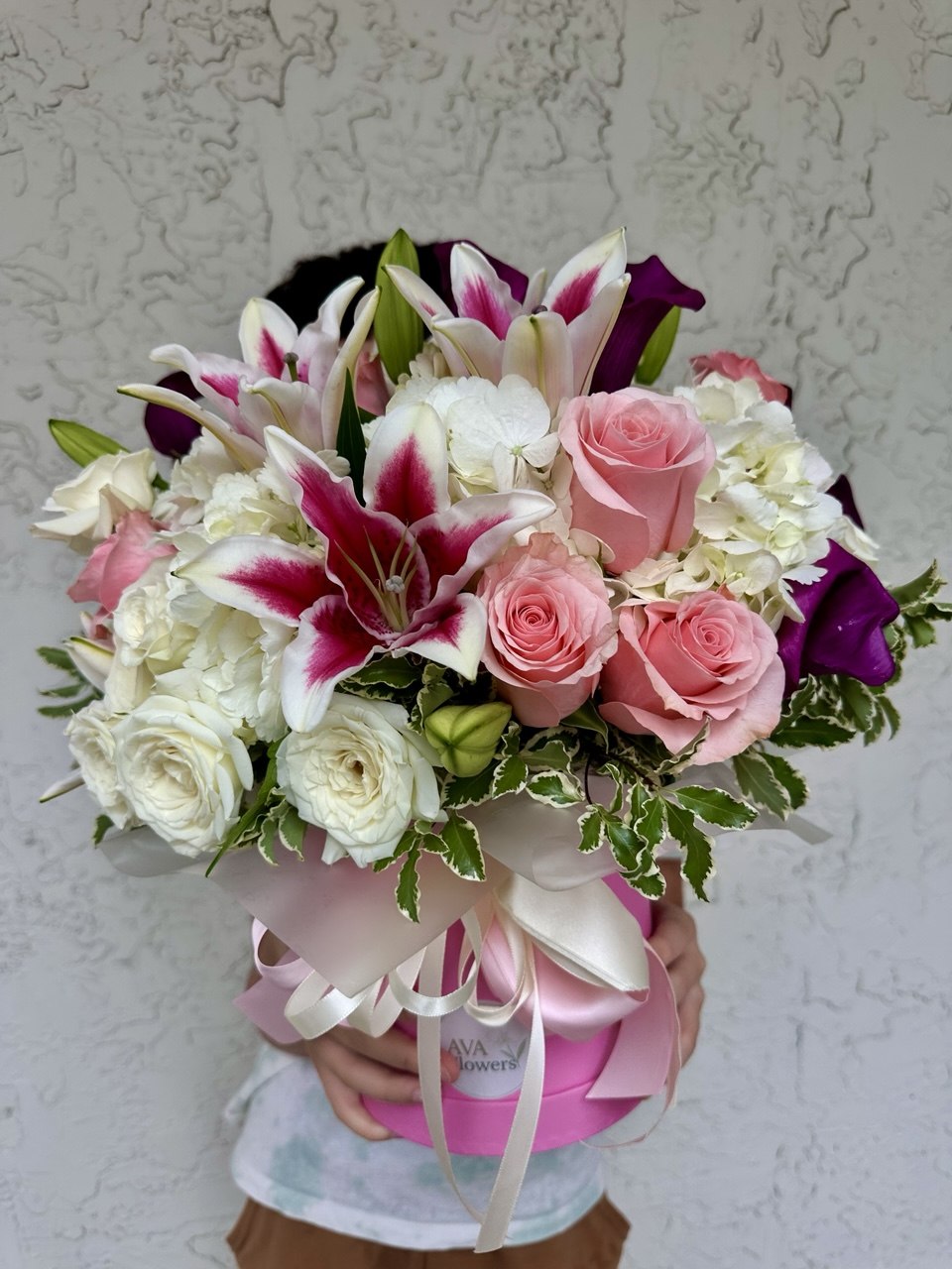 Bouquet of flowers with pink, white, and purple colors held against a textured wall.