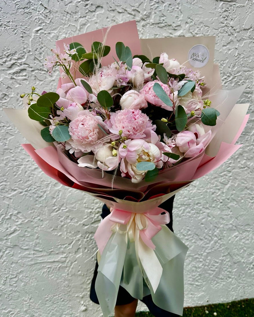Bouquet of pink flowers with greenery on a textured white wall