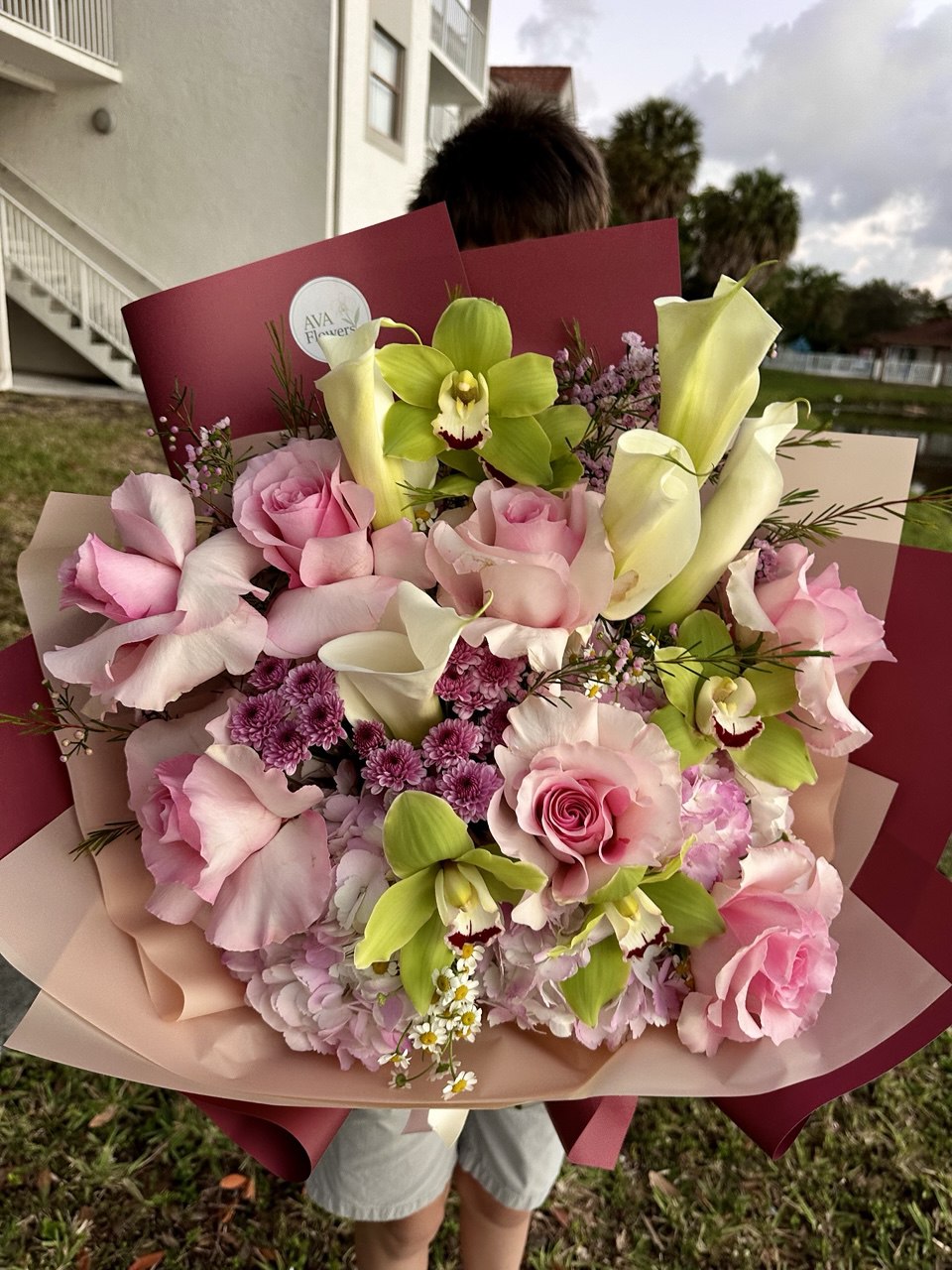 Bouquet of flowers held by a person outdoors with a building and trees in the background