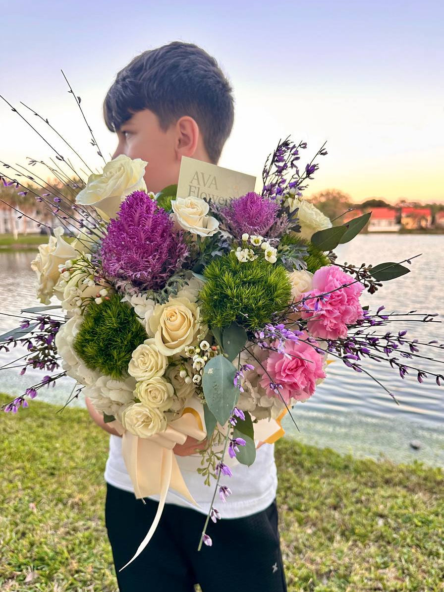 Person holding a bouquet of flowers by a waterfront at sunset