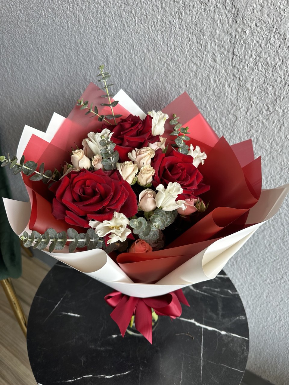 Chic hand-tied bouquet with red roses, delicate white lisianthus, blush spray roses and eucalyptus, wrapped in red and white designer paper with satin ribbon.