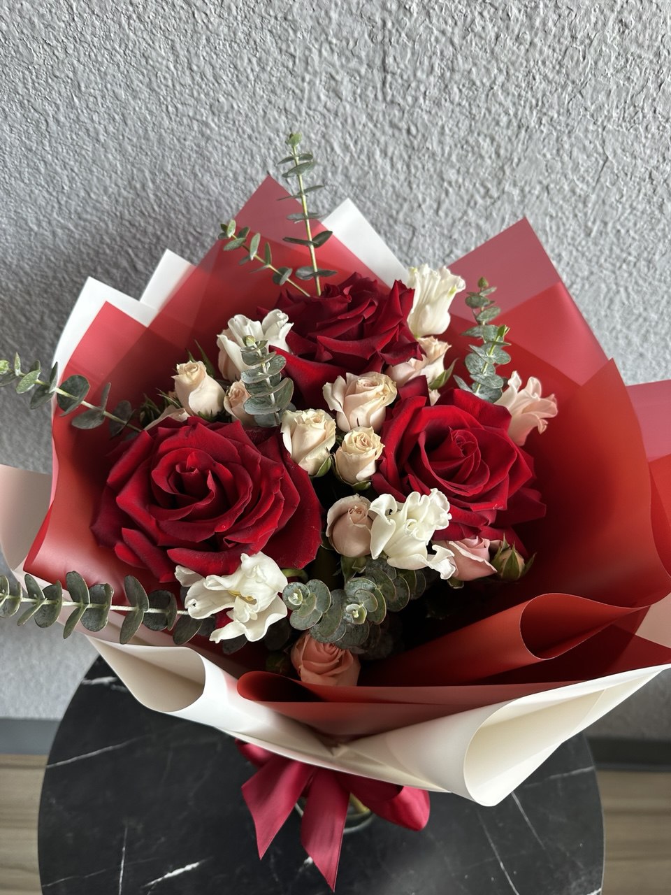 Chic hand-tied bouquet with red roses, delicate white lisianthus, blush spray roses and eucalyptus, wrapped in red and white designer paper with satin ribbon.