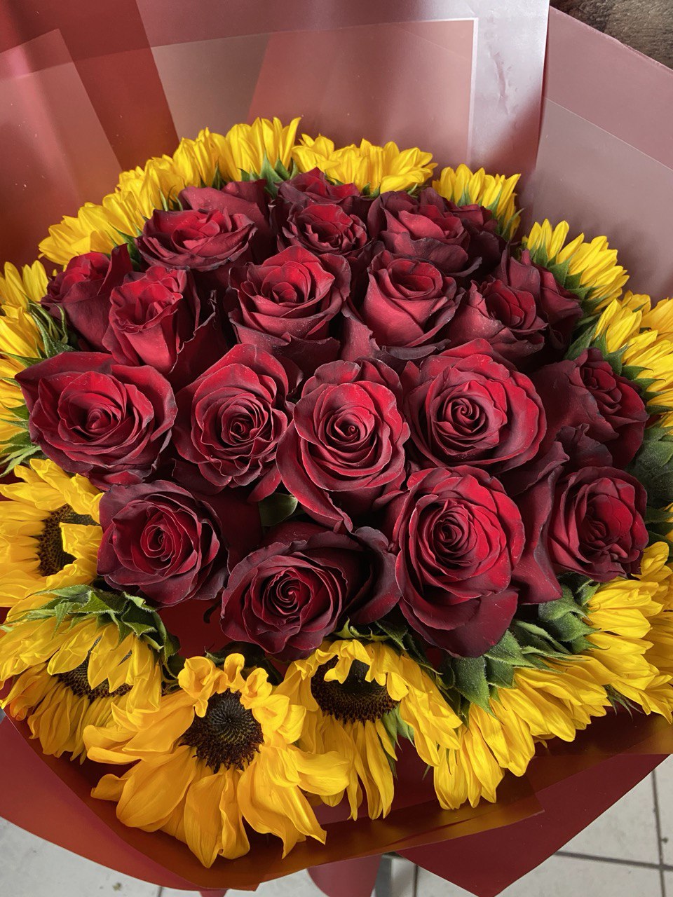 Vibrant bouquet with deep red roses surrounded by bright yellow sunflowers, wrapped in burgundy paper with matching ribbons.