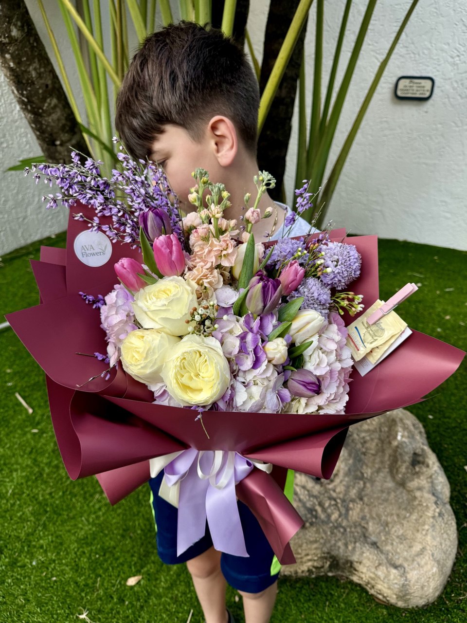 Child holding a bouquet of flowers with a decorative ribbon on a grassy background
