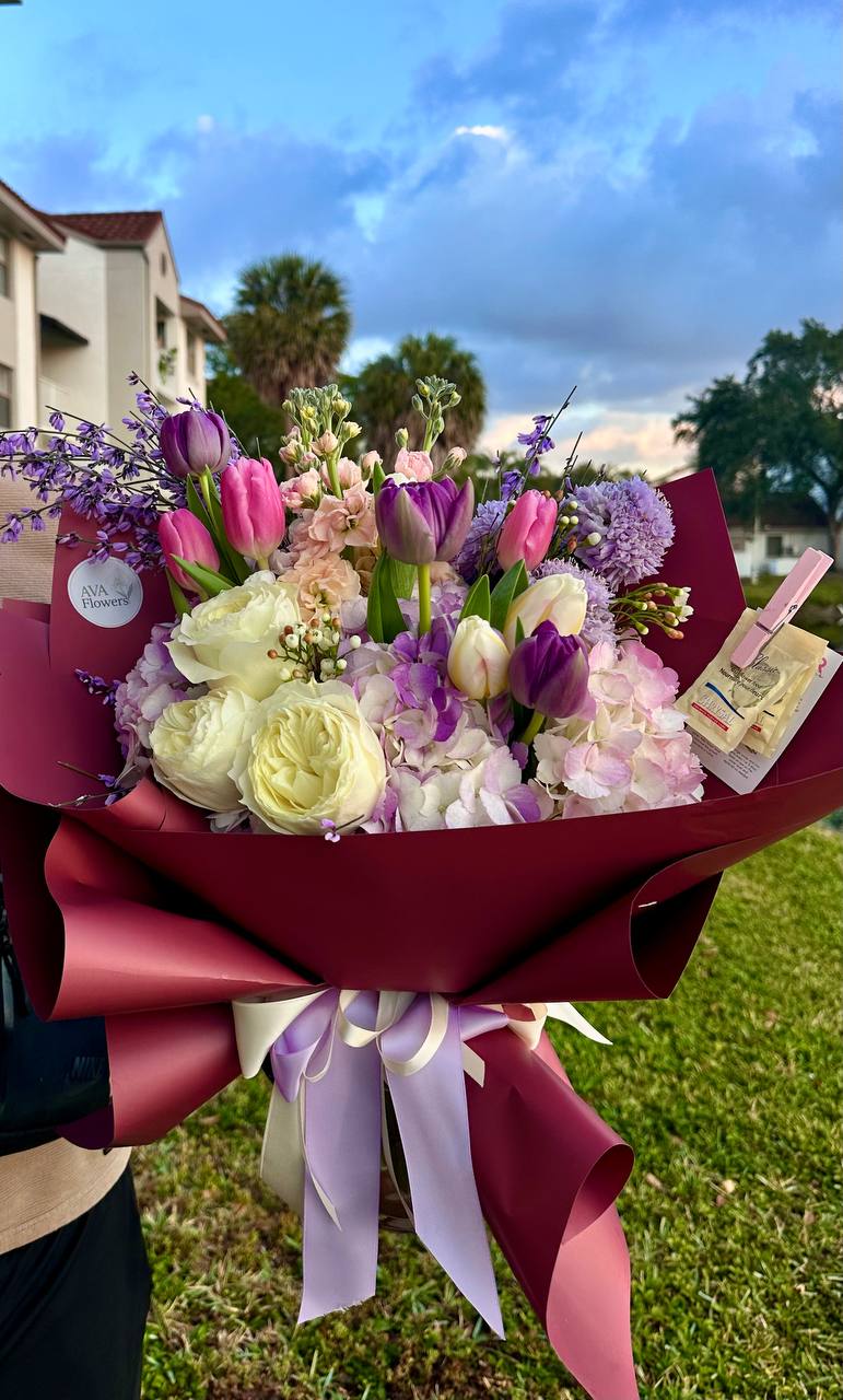Bouquet of flowers with a red wrap held outdoors.